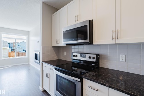 Kitchen featuring white shaker-style cabinetry with brushed nickel hardware, dark granite-finish countertops, and a subway tile backsplash - 17707 59 Street Nw, Edmonton, AB - Indoor Photo Showing Kitchen With Stainless Steel Kitchen With Upgraded Kitchen