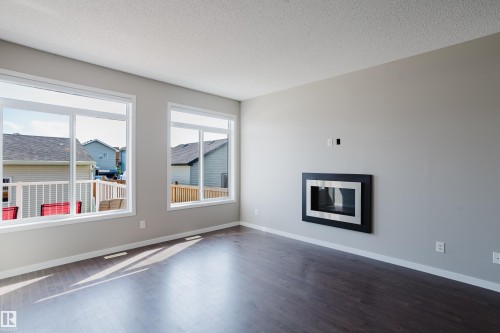 Spacious room featuring multiple large windows, dark wood-finish flooring, and a modern wall-mounted fireplace with a black and stainless steel frame - 17707 59 Street Nw, Edmonton, AB - Indoor Photo Showing Living Room