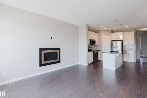 Open-concept living area featuring dark wood-finish flooring, a contemporary electric fireplace with a black surround, and white baseboards - 17707 59 Street Nw, Edmonton, AB - Indoor