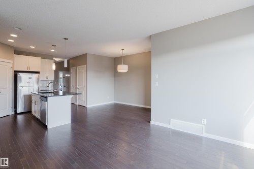 Open-concept living space featuring wood-finish flooring, a kitchen island with a sink and pendant lighting, stainless steel appliances, and white cabinetry - 17707 59 Street Nw, Edmonton, AB - Indoor Photo Showing Kitchen