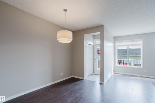 Spacious interior featuring a tiered drum pendant light, dark wood-finish flooring, a white-trimmed window, light grey walls, and white baseboards - 17707 59 Street Nw, Edmonton, AB - Indoor Photo Showing Other Room