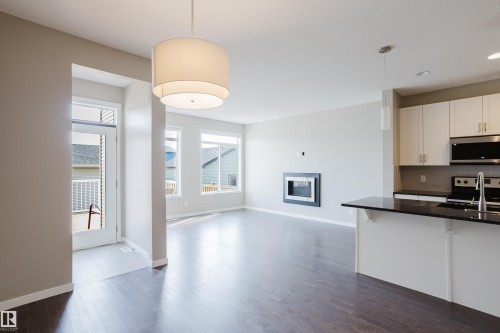 Open-concept living space with dark wood-finish flooring, a modern electric fireplace, and multiple large windows - 17707 59 Street Nw, Edmonton, AB - Indoor Photo Showing Kitchen