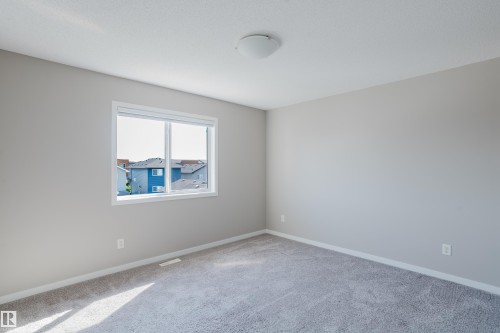 Spacious room featuring neutral-toned walls, plush gray carpeting, and a large window with white trim - 17707 59 Street Nw, Edmonton, AB - Indoor Photo Showing Other Room