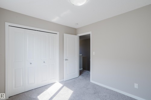 Spacious room featuring neutral carpeting, light gray walls, a white bi-fold closet, a white interior door, and a flush mount ceiling light fixture - 17707 59 Street Nw, Edmonton, AB - Indoor