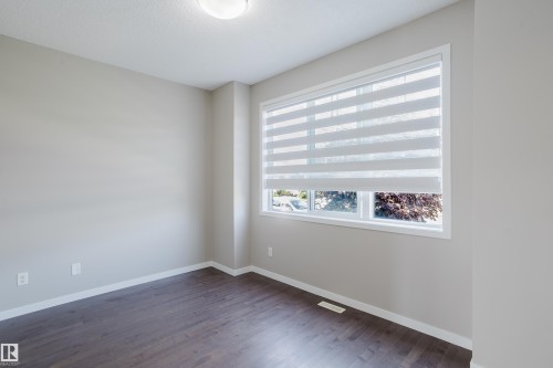 Spacious room featuring wood-finish flooring, light neutral wall paint, and a large window with privacy blinds - 17707 59 Street Nw, Edmonton, AB - Indoor Photo Showing Other Room
