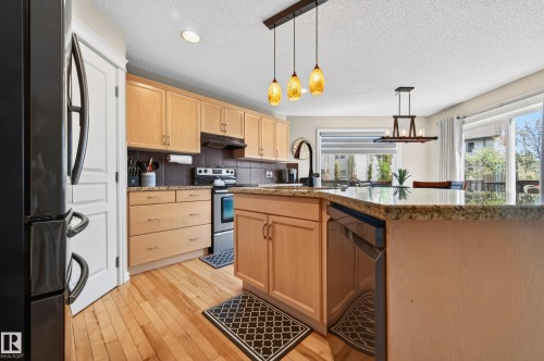 Kitchen featuring wood-finish flooring, light wood cabinetry, stone countertops, a tiled backsplash, and stainless steel appliances - 9 Snowbird Crescent, Leduc, AB - Indoor Photo Showing Kitchen