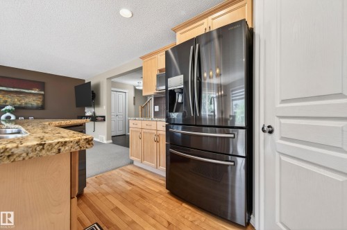 Kitchen featuring wood-finish flooring, light wood cabinetry, granite-finish countertops, and a black stainless steel refrigerator - 9 Snowbird Crescent, Leduc, AB - Indoor Photo Showing Kitchen With Double Sink