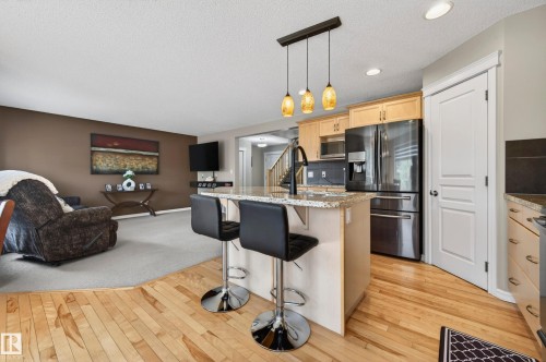Open-concept kitchen and living area featuring wood-finish flooring, a kitchen island with stone countertop, natural wood cabinetry, and stainless steel appliances - 9 Snowbird Crescent, Leduc, AB - Indoor Photo Showing Kitchen With Upgraded Kitchen