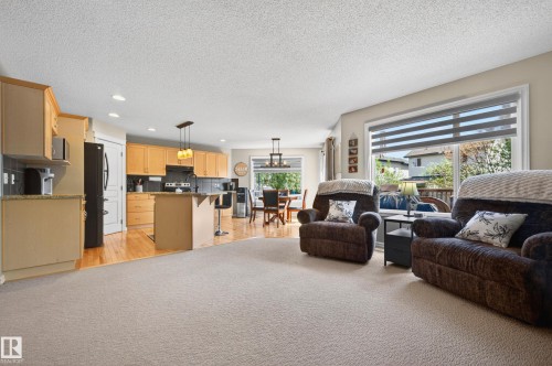 Open-concept living area featuring light-toned carpeting, a kitchen with light wood cabinetry, stone-finish countertops, and black appliances, and a dining area with a contemporary chandelier - 9 Snowbird Crescent, Leduc, AB - Indoor Photo Showing Other Room