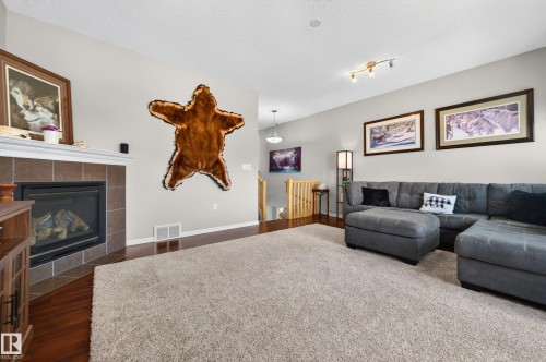 Spacious living area featuring wood-finish flooring, a tiled fireplace with a white mantel, and a neutral color palette - 9 Snowbird Crescent, Leduc, AB - Indoor Photo Showing Living Room With Fireplace