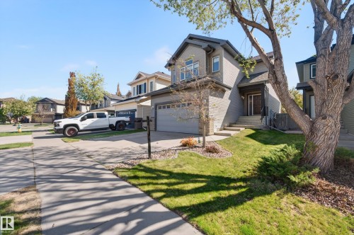 Two-story residence featuring a gray facade with stone accents, an attached garage, a paved driveway, and a welcoming front entrance with a covered porch - 9 Snowbird Crescent, Leduc, AB - Outdoor With Facade