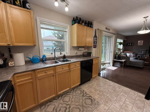 Kitchen featuring light wood-finish cabinetry, a double basin stainless steel sink with a gooseneck faucet, black appliances, and durable tile flooring - #93 12050 17 Av Sw, Edmonton, AB - Indoor Photo Showing Kitchen With Double Sink