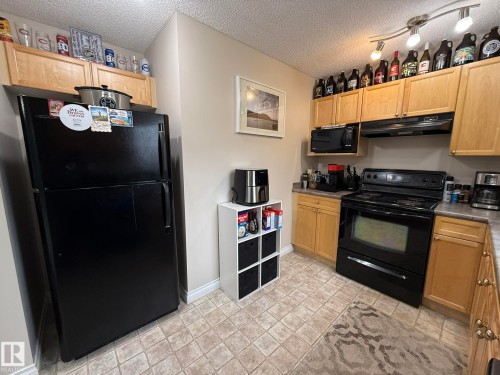 Kitchen featuring light wood cabinetry, black appliances, textured countertop, and track lighting - #93 12050 17 Av Sw, Edmonton, AB - Indoor Photo Showing Kitchen