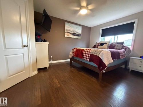 Spacious room featuring wood-finish flooring, a ceiling fan with integrated lighting, a large window with a roller shade, and warm-toned wall paint - #93 12050 17 Av Sw, Edmonton, AB - Indoor Photo Showing Bedroom