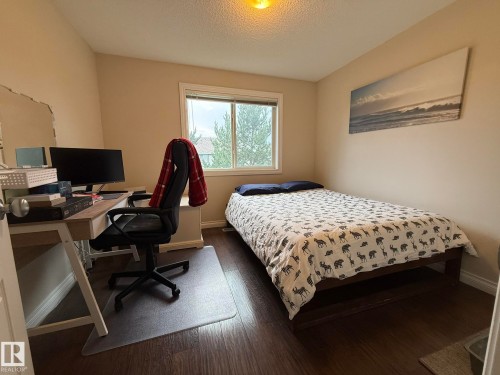 Neutral-toned walls complement wood-finish flooring in this room featuring a window with white trim, offering exterior views - #93 12050 17 Av Sw, Edmonton, AB - Indoor Photo Showing Bedroom