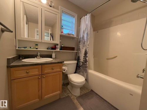 Bathroom featuring a vanity with wood-finish cabinetry, a white drop-in sink, and a dark countertop - #93 12050 17 Av Sw, Edmonton, AB - Indoor Photo Showing Bathroom
