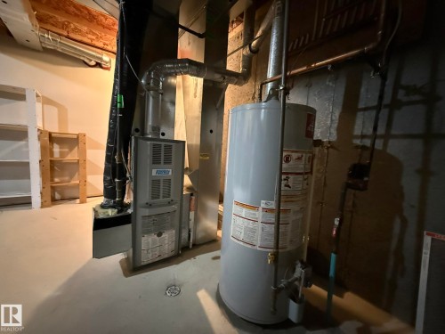 Utility room featuring a water heater and furnace with exposed ductwork, concrete flooring, and bare wood ceiling joists - #93 12050 17 Av Sw, Edmonton, AB - Indoor Photo Showing Basement