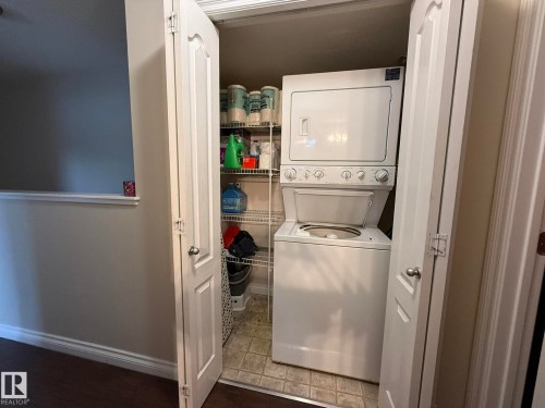 Dedicated laundry closet featuring a stacked white washer and dryer unit, bi-fold doors, and neutral-toned floor tile - #93 12050 17 Av Sw, Edmonton, AB - Indoor Photo Showing Laundry Room