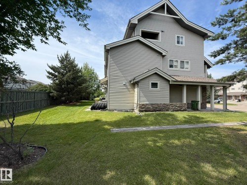 Two-story residence featuring light gray siding, a covered porch with stone detailing, multiple windows, and a generously sized grassy side yard - #93 12050 17 Av Sw, Edmonton, AB - Outdoor With Deck Patio Veranda