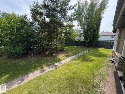 Expansive rear yard featuring a wooden privacy fence, mature trees, and a stone veneer foundation accenting the home's exterior - #93 12050 17 Av Sw, Edmonton, AB - Outdoor