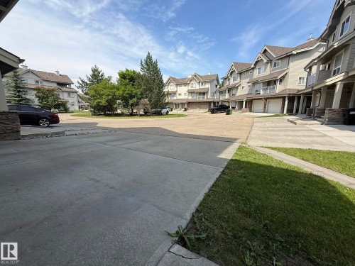 Concrete paved driveway with surrounding townhomes featuring light-colored siding, dark roofing, and individual garage doors - #93 12050 17 Av Sw, Edmonton, AB - Outdoor