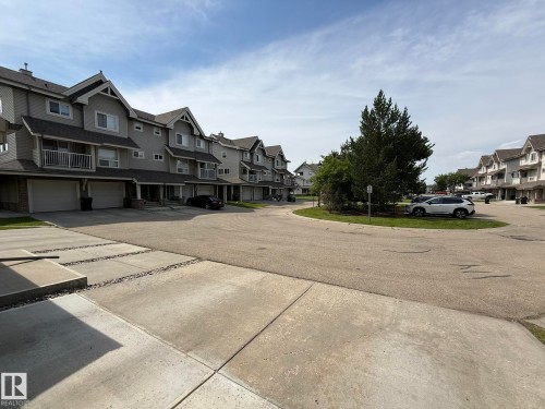 Townhouse exterior featuring gray siding, stone accents, multiple gables, and individual garages - #93 12050 17 Av Sw, Edmonton, AB - Outdoor With Facade