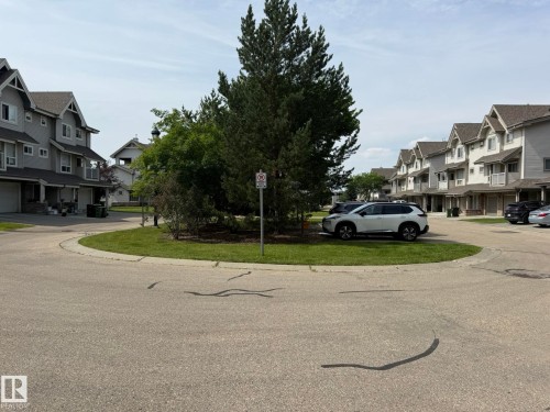Residential street featuring a central landscaped island with mature trees and shrubbery - #93 12050 17 Av Sw, Edmonton, AB - Outdoor With Facade