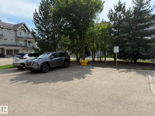 Paved parking area with mature trees and a multi-level residential building in the background - #93 12050 17 Av Sw, Edmonton, AB - Outdoor