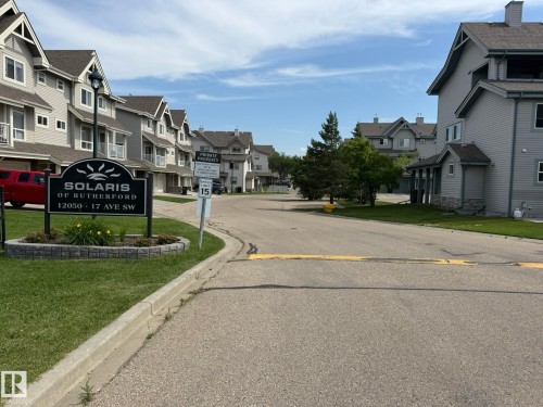 Entryway featuring a stone-clad sign, manicured landscaping, and a street lamp - #93 12050 17 Av Sw, Edmonton, AB - Outdoor With Facade