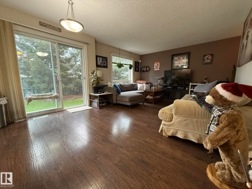Living area featuring wood-finish flooring, a contemporary ceiling light fixture, a sliding glass door providing exterior access, and a large window - #93 12050 17 Av Sw, Edmonton, AB - Indoor Photo Showing Living Room