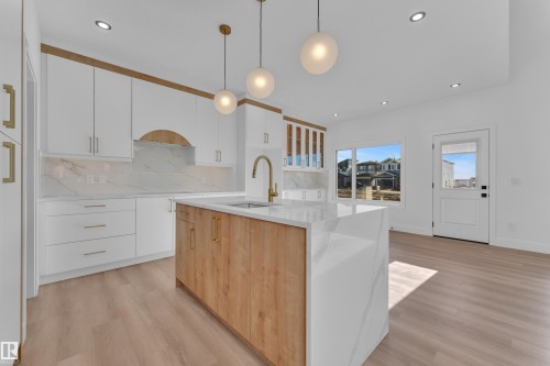 Contemporary kitchen featuring a large central island with a waterfall edge, a gold-finish faucet, and coordinating pendant lighting - 382 Linden Loop, Leduc, AB - Indoor Photo Showing Kitchen With Upgraded Kitchen