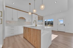 Contemporary kitchen featuring a large central island with a waterfall edge, a gold-finish faucet, and coordinating pendant lighting - 