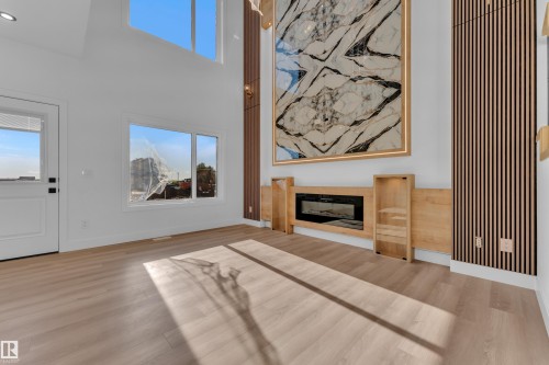 Vaulted ceilings with upper windows, wood-finish flooring, a built-in electric fireplace with surrounding cabinetry, and a feature wall with vertical wood slats - 382 Linden Loop, Leduc, AB - Indoor Photo Showing Living Room With Fireplace