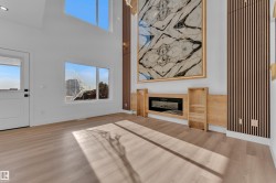 Vaulted ceilings with upper windows, wood-finish flooring, a built-in electric fireplace with surrounding cabinetry, and a feature wall with vertical wood slats - 