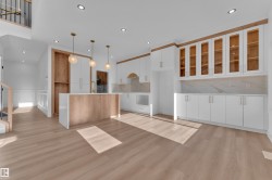 Open-concept kitchen and dining area featuring light wood-finish flooring, a central island with a gold-tone faucet, white cabinetry with gold-tone hardware, a white countertop, and a marble-patterned backsplash - 