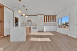 Modern kitchen featuring a waterfall island with stone countertop, white cabinetry, wood-finish accents, recessed lighting, and large windows - 