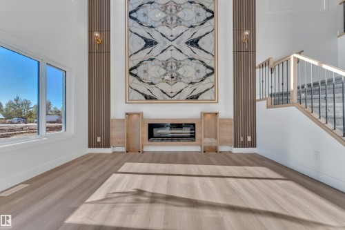 Vaulted ceiling living space featuring a contemporary fireplace with a large decorative panel, recessed electric fireplace, and light wood-finish flooring - 382 Linden Loop, Leduc, AB - Indoor With Fireplace