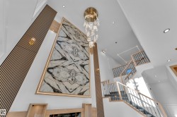 Grand entryway featuring a multi-story natural stone accent wall, a contemporary chandelier, recessed lighting, and a modern staircase with wood handrails and black metal balusters - 