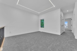 Spacious carpeted room featuring a contemporary linear ceiling light fixture, a window opening, and a railing with vertical spindles - 