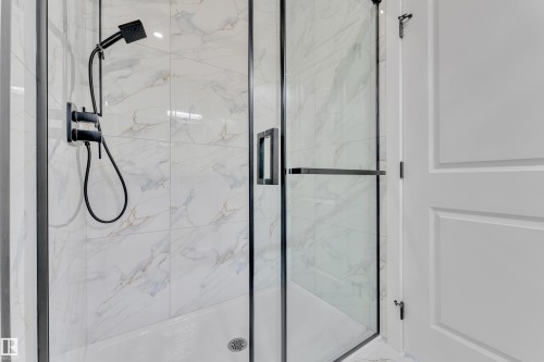 Modern shower enclosure featuring a frameless glass door with black trim, matte black shower fixtures, and white tile with subtle marbling - 382 Linden Loop, Leduc, AB - Indoor Photo Showing Bathroom