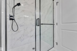 Modern shower enclosure featuring a frameless glass door with black trim, matte black shower fixtures, and white tile with subtle marbling - 