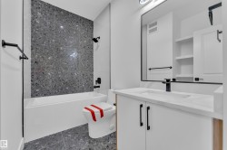Bathroom featuring a bathtub with a tiled shower surround, a white vanity with a countertop, an integrated sink, a large framed mirror, and matte black fixtures - 