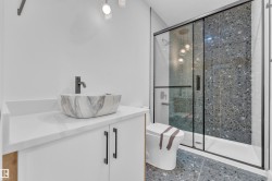 Contemporary bathroom featuring a vessel sink with a matte black faucet, white shaker-style vanity, and a shower with a dark speckled tile surround behind clear glass doors with black framing - 