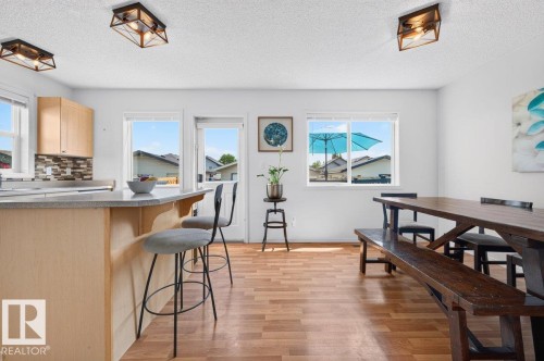 Open-concept living space featuring wood-finish flooring, a kitchen island with seating, a glass door to the exterior, and ample natural light from multiple windows - 17411 90 Street Nw, Edmonton, AB - Indoor Photo Showing Dining Room