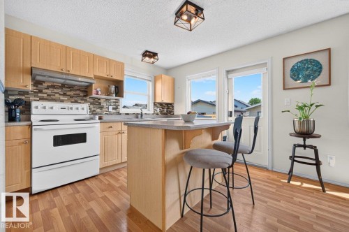 Kitchen featuring wood-finish flooring, light wood cabinetry, a tile backsplash, and an island with seating - 17411 90 Street Nw, Edmonton, AB - Indoor Photo Showing Kitchen