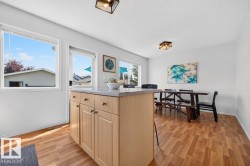 Open-concept dining area featuring wood-finish flooring, a central island with light wood cabinetry and a light-toned countertop, and multiple windows providing ample natural light - 