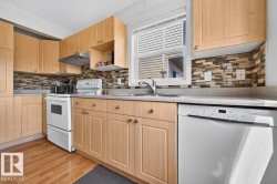 Kitchen featuring light wood-finish cabinetry, a mosaic tile backsplash, a stainless steel sink with a single-handle faucet, a white dishwasher, and wood-finish flooring - 