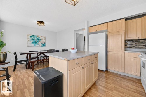 Kitchen featuring wood-finish flooring, light wood cabinetry, a mosaic tile backsplash, and a central island with a light-toned countertop - 17411 90 Street Nw, Edmonton, AB - Indoor Photo Showing Kitchen
