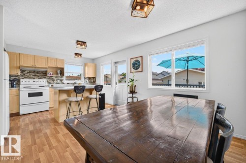 Open-concept kitchen and dining area featuring wood-finish flooring, light wood cabinetry, a tiled backsplash, and a breakfast bar - 17411 90 Street Nw, Edmonton, AB - Indoor