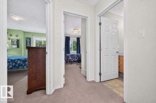 Carpeted hallway providing access to three distinct spaces, including a room with a double window and a bathroom with a wood-finish vanity - 17411 90 Street Nw, Edmonton, AB - Indoor